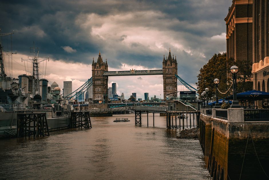The image displays London's Tower Bridge illuminated at night, with its distinctive twin towers and suspension design reflected in the calm River Thames below. The bridge’s intricate stonework and m