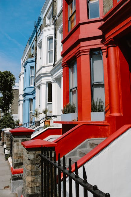 Photograph of colorful terraced residential buildings on Portobello Road, Notting Hill, London, featuring a row of Victorian-style houses with decorative facades. The houses are painted in pastel shad